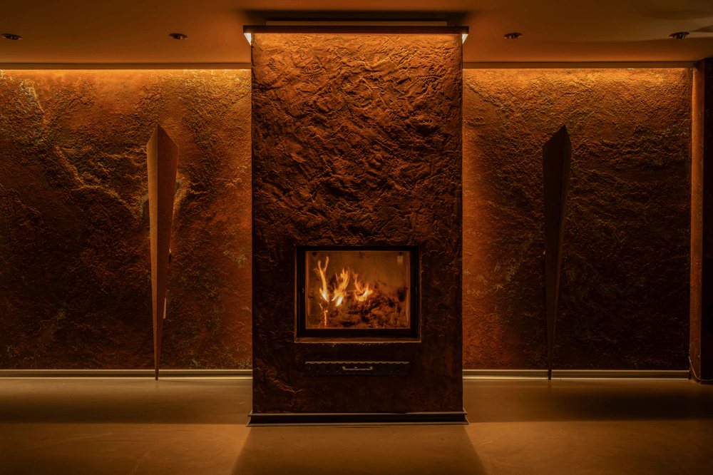 Ein beleuchteter Kamin mit loderndem Feuer in einer dunklen Steinwand